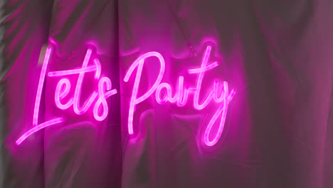 Close-Up-Of-Photo-Booth-With-Neon-"Let's-Party"-Sign-Hanging-Outside